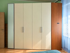 Ein Zimmer mit großem Kleiderschrank, Holztür und einem Fenster mit transparenten Vorhängen.