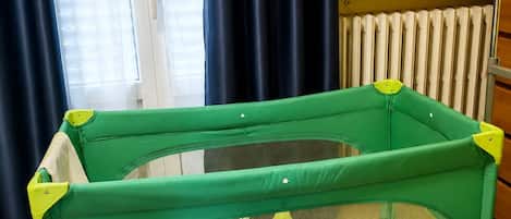 A green baby playpen with a mesh side, a plush toy, and a patterned mat inside.