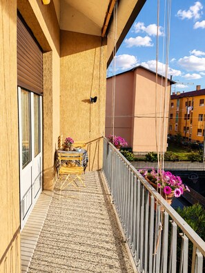 Ein Balkon mit Tisch und Stühlen, ein Fenster und Blick auf benachbarte Gebäude.