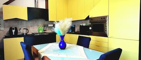 A modern kitchen with yellow cabinets, a dining table with chairs, and a blue vase with a plant.