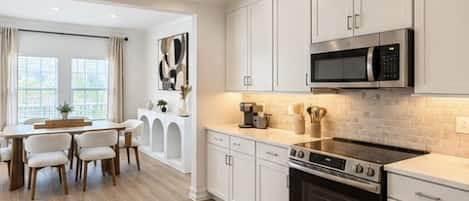 A modern kitchen with white cabinetry, a stainless steel microwave, and a black stove.
