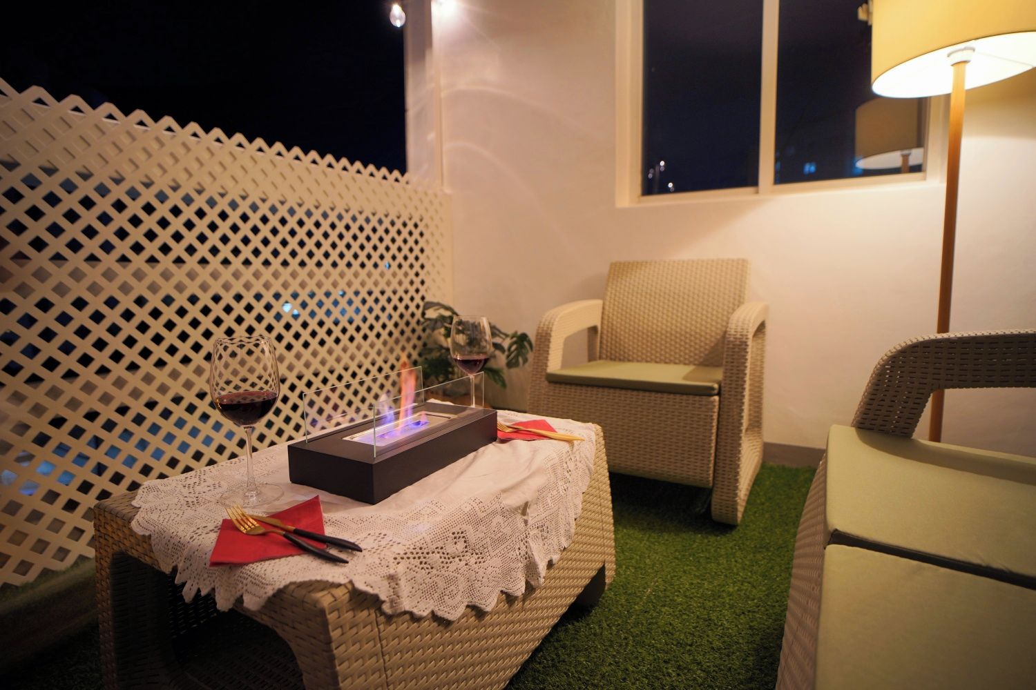 A cozy outdoor seating area with wicker furniture, a table with a lace tablecloth, and a decorative fire feature.