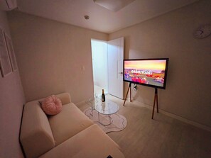 Ein Wohnzimmer mit einer Couch, einem Glastisch, einem Flachbildfernseher auf einem Schrank und einer Tür, die in einen anderen Raum führt.
