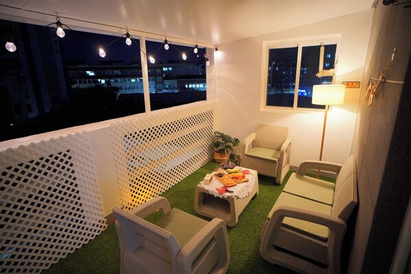 A balcony with outdoor seating, a table with food and drinks, and a view of the city at night.