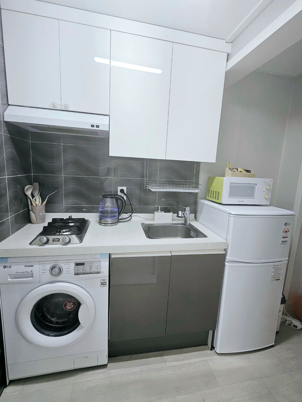 A compact kitchen with a washing machine, a microwave, a gas stove, and a sink.