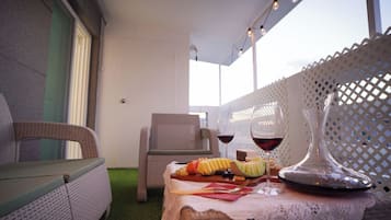 Un rincón exterior acogedor con sillas de mimbre, una mesa con aperitivos y copas de vino, y un jarrón decorativo.