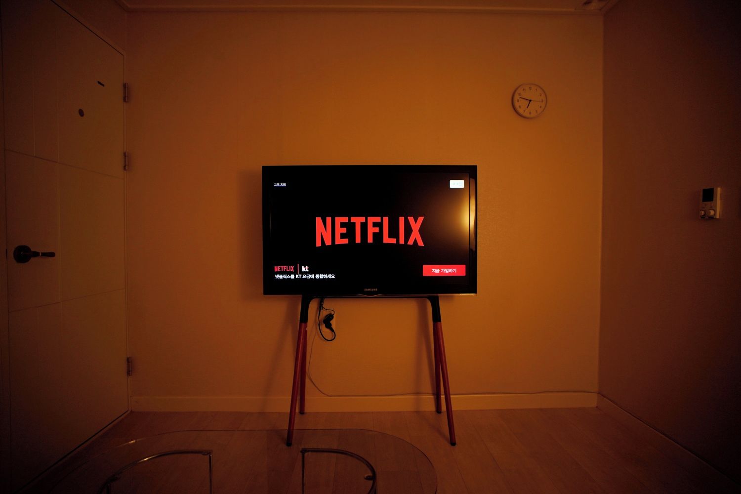 Un televisor montado en un soporte en una habitación con una puerta y un reloj en la pared.