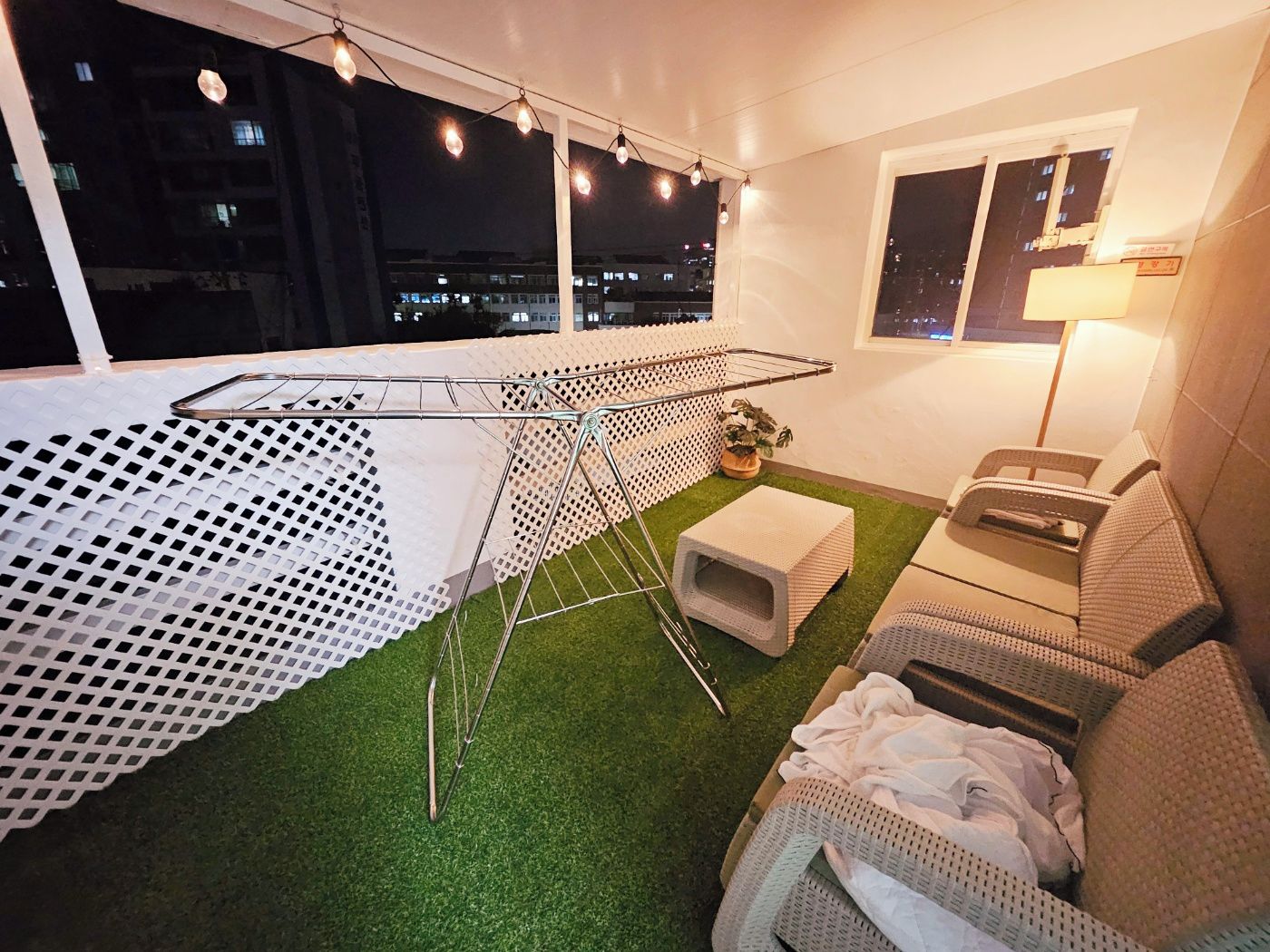 A room with a small table, a pet bed, and a sofa. There is a window with a view of buildings outside.