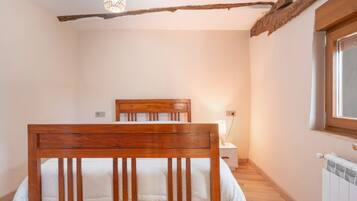 Un dormitorio con una cama de madera, una mesita de noche con lámpara, un radiador y una ventana.