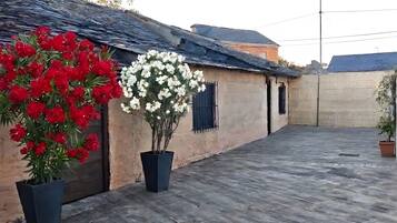 Een binnenplaats met een houten vloer, twee potplanten met rode en witte bloemen, en een gebouw met een pannendak.