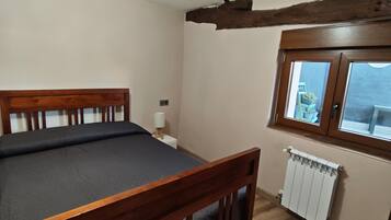 Una habitación con cama de madera, un radiador, una ventana y una lámpara en el techo.