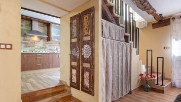 A kitchen with wooden cabinets and a stone backsplash, a staircase with a decorative door, and a view of the living area.