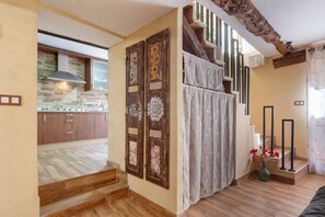 A kitchen with wooden cabinets and a stone backsplash, a staircase with a decorative door, and a view of the living area.