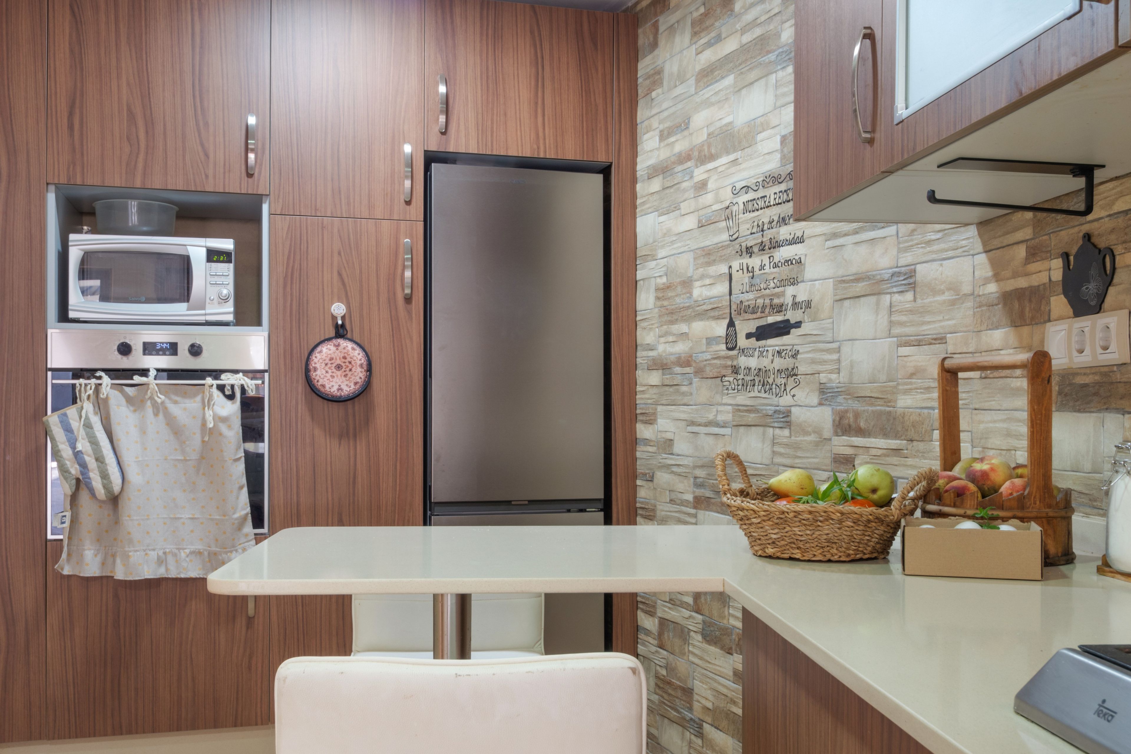 A modern kitchen with wooden cabinets, a stainless steel refrigerator, a microwave, and a stone backsplash.