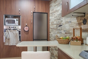 A modern kitchen with wooden cabinets, a stainless steel refrigerator, a microwave, and a stone backsplash.