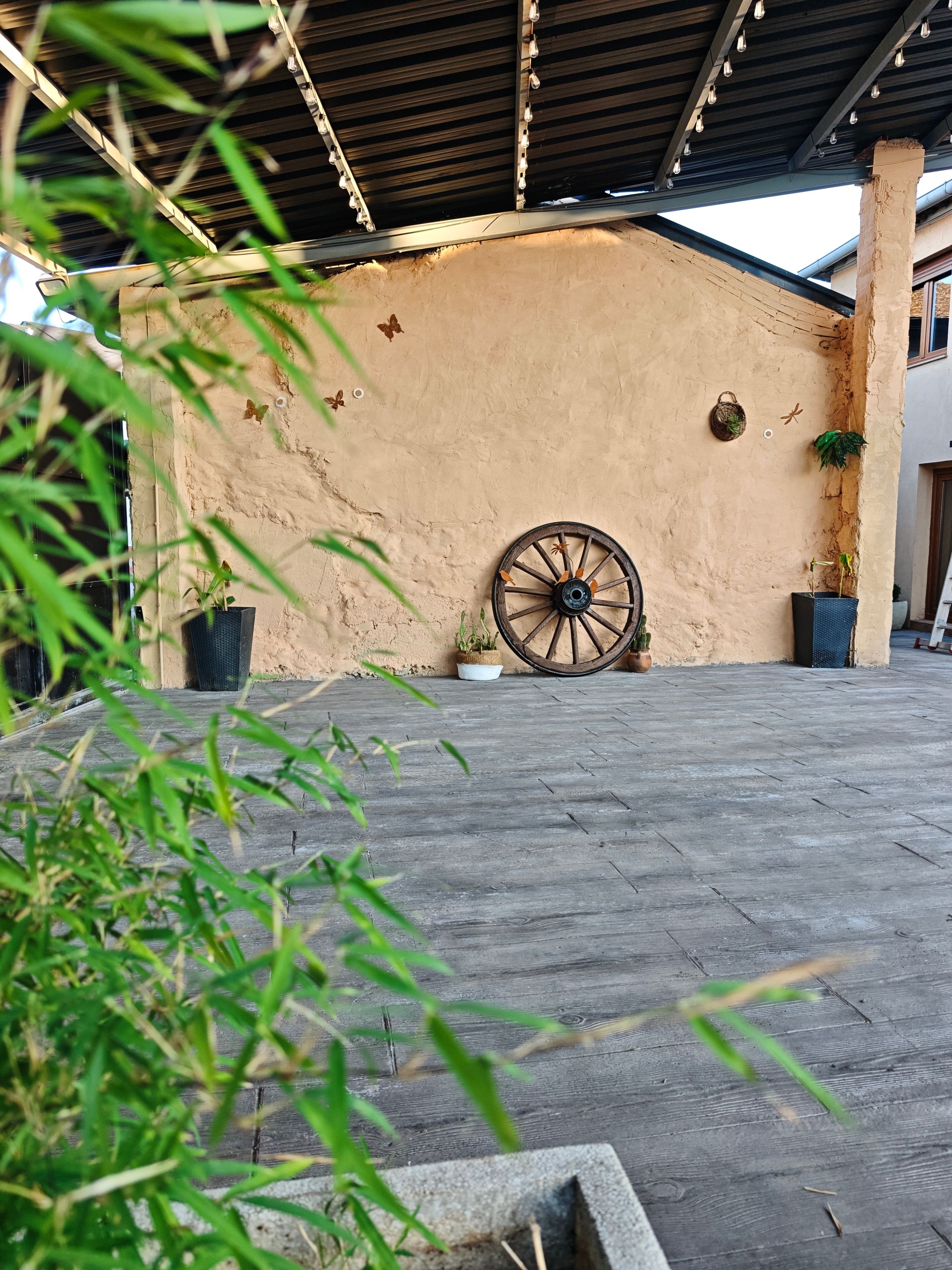 Un espace extérieur agrémenté d’un mur rustique, d’une décoration en forme de roue en bois et de plantes en pot.