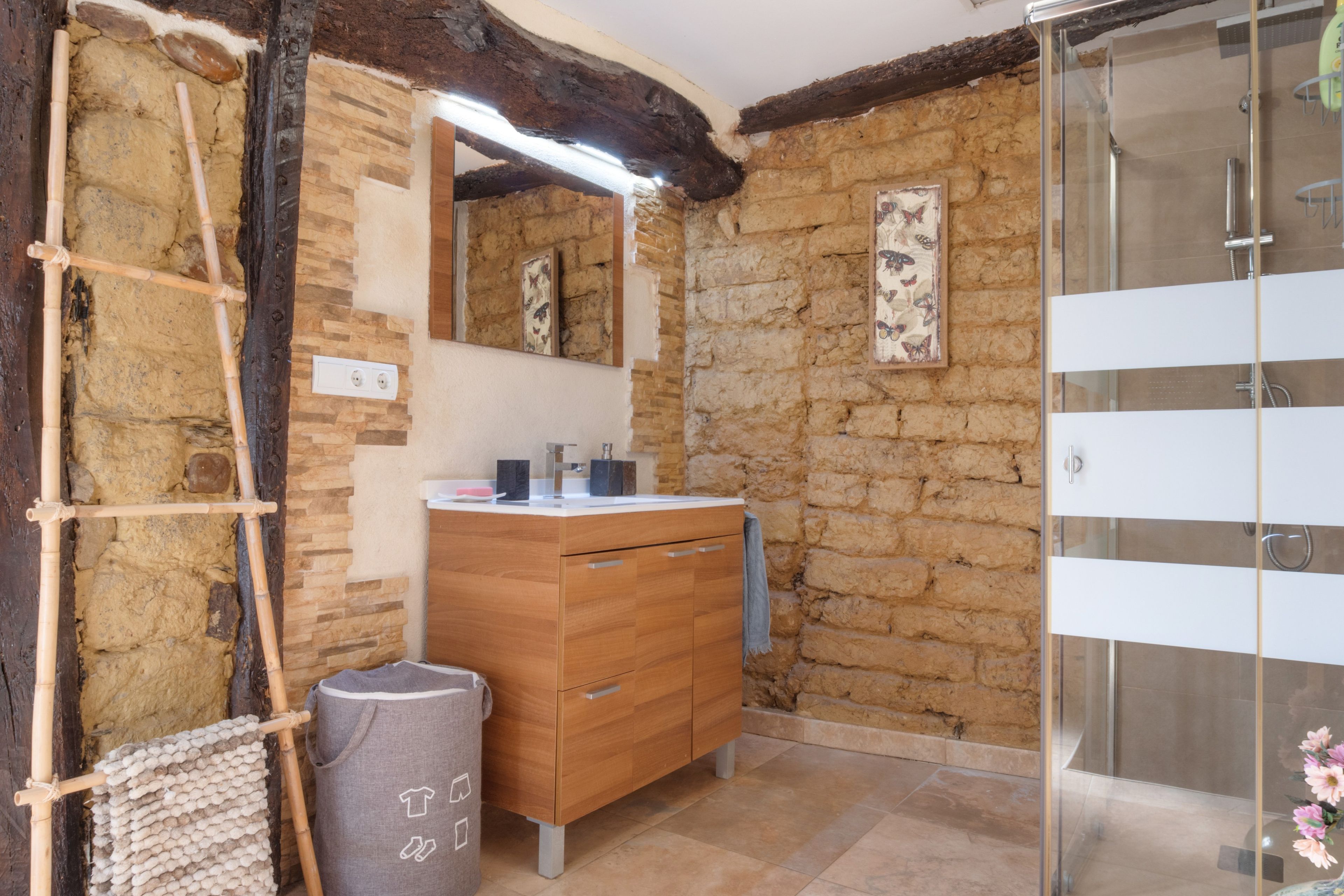 Een badkamer met een stenen muur, een houten wastafelmeubel, een douchecabine van glas en een spiegel.