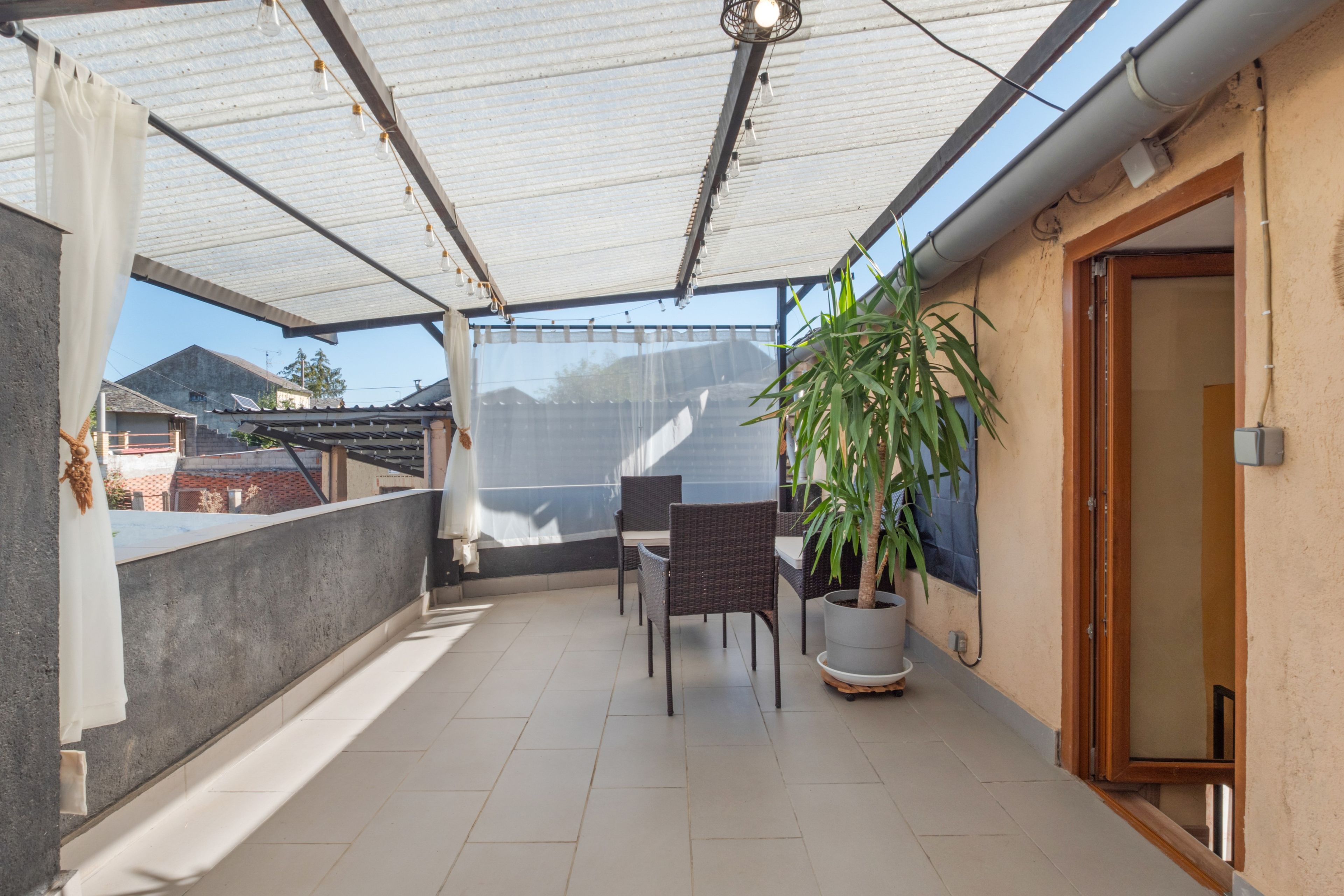 Een overdekt balkon met een tafel en stoelen, een bloempot en uitzicht op de omgeving.