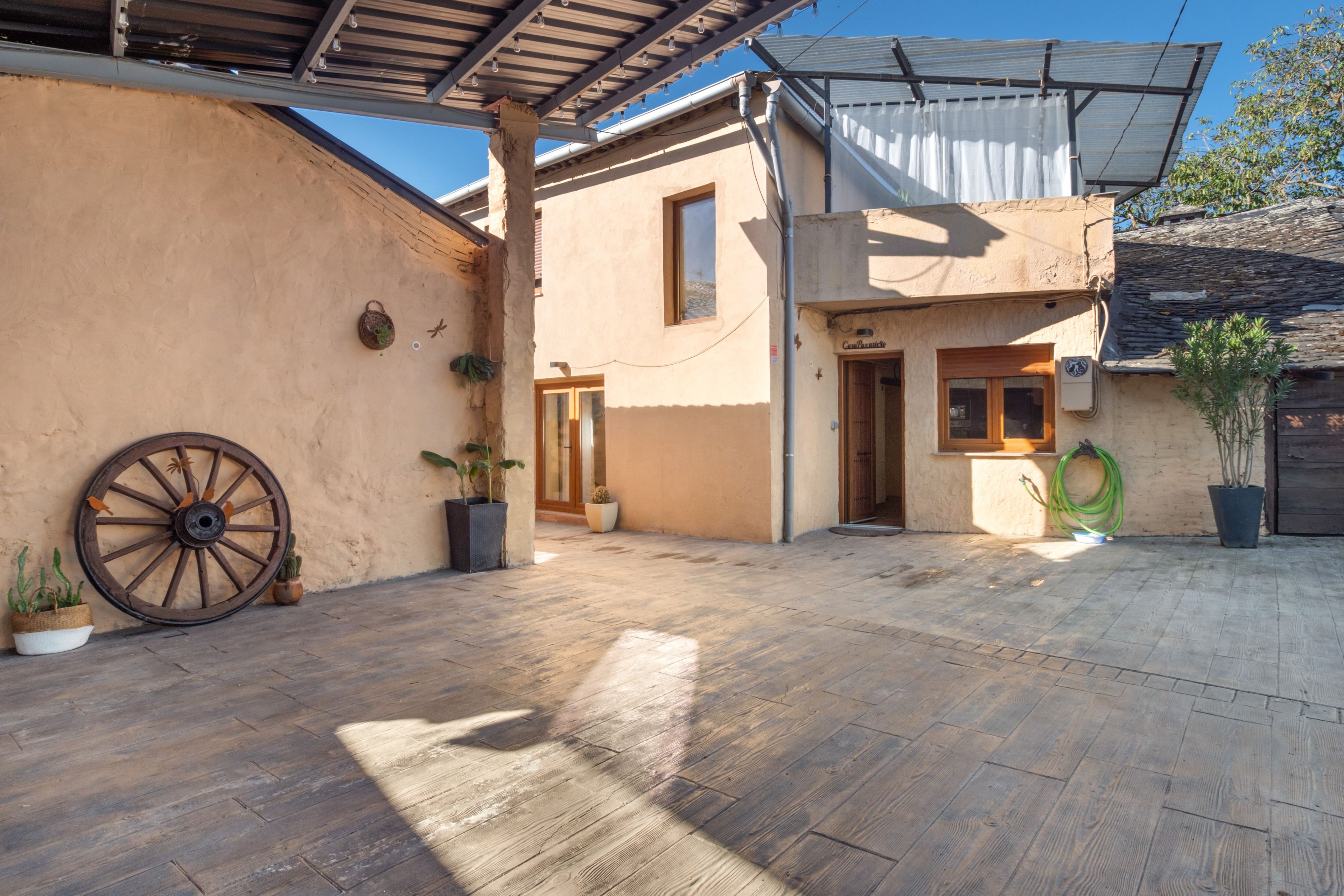 Un patio con piso de madera, una rueda grande y plantas en macetas.