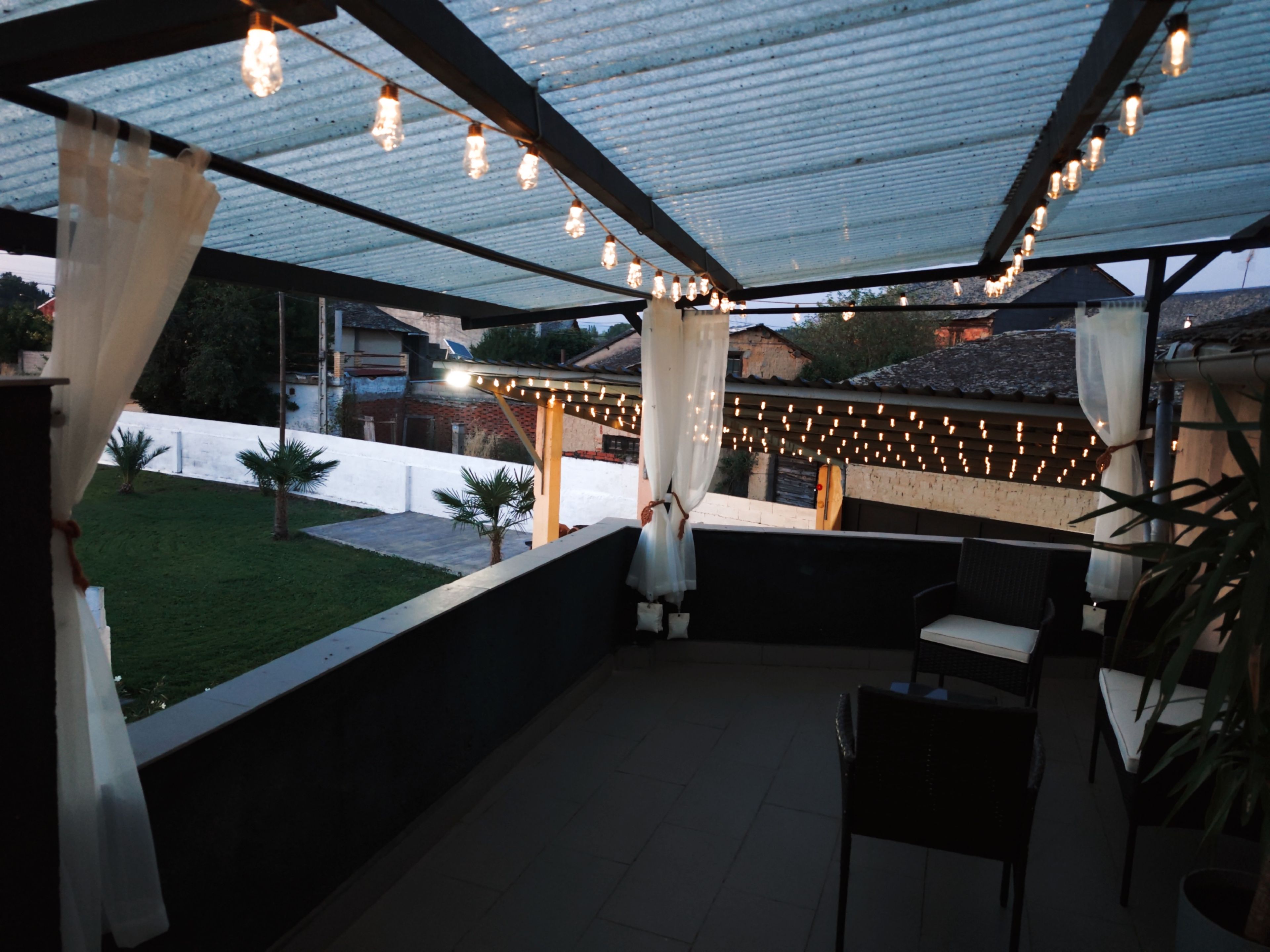 Un patio al aire libre con luces colgantes, una zona de estar cubierta y vistas del vecindario.