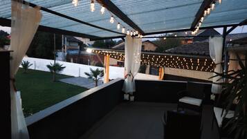 Un patio al aire libre con luces colgantes, una zona de estar cubierta y vistas del vecindario.
