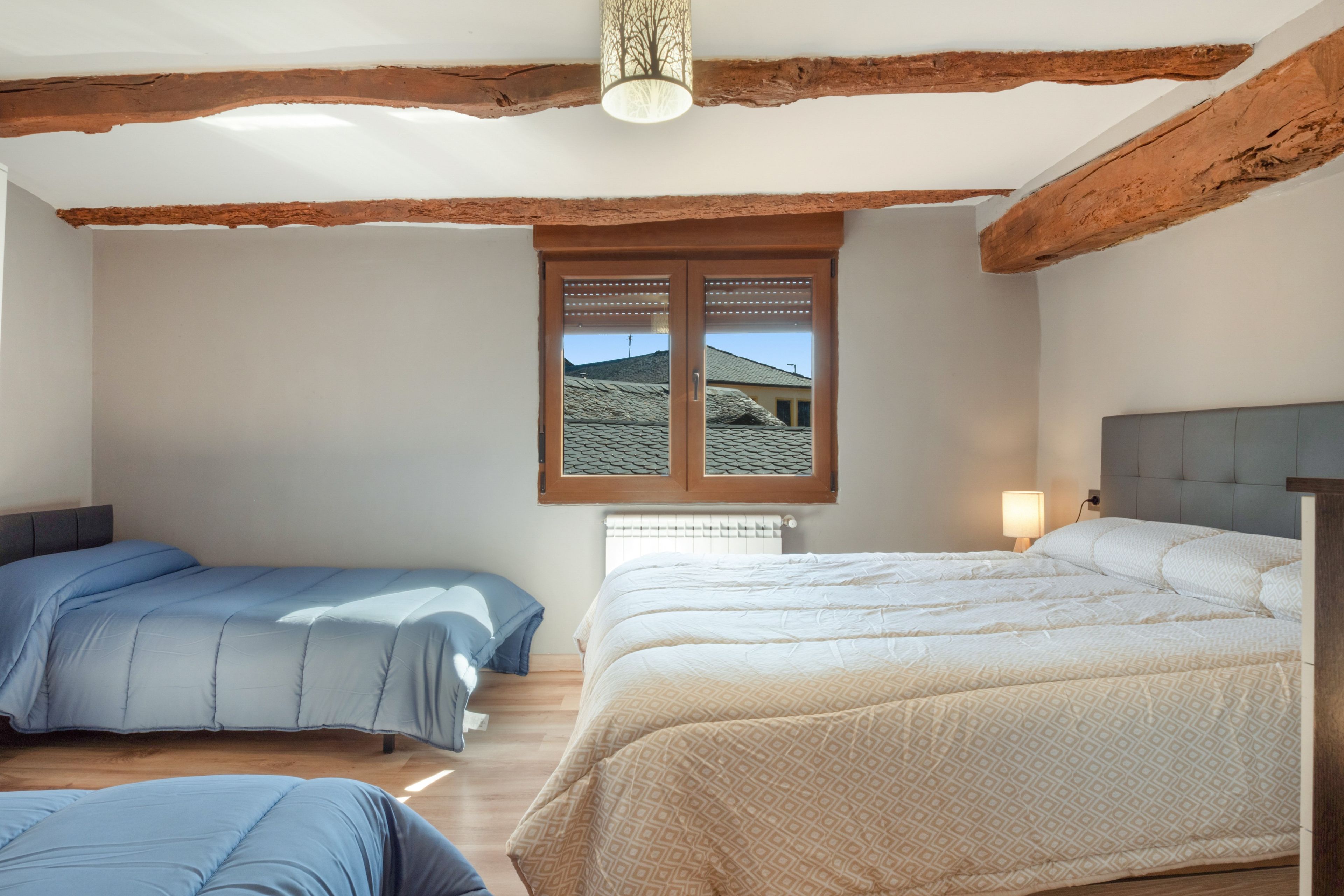 Une chambre avec deux lits, des poutres en bois au plafond, une fenêtre avec des volets et un radiateur.