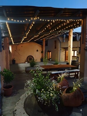 Een terras buiten met lichtjes, een houten tafel en potplanten.