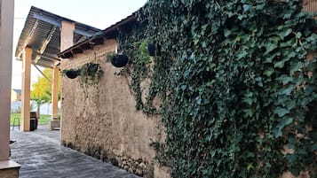 Un espace extérieur abrité doté d’un plancher en bois, d’un mur en pierre recouvert de lierre et d’une structure de toit en métal.