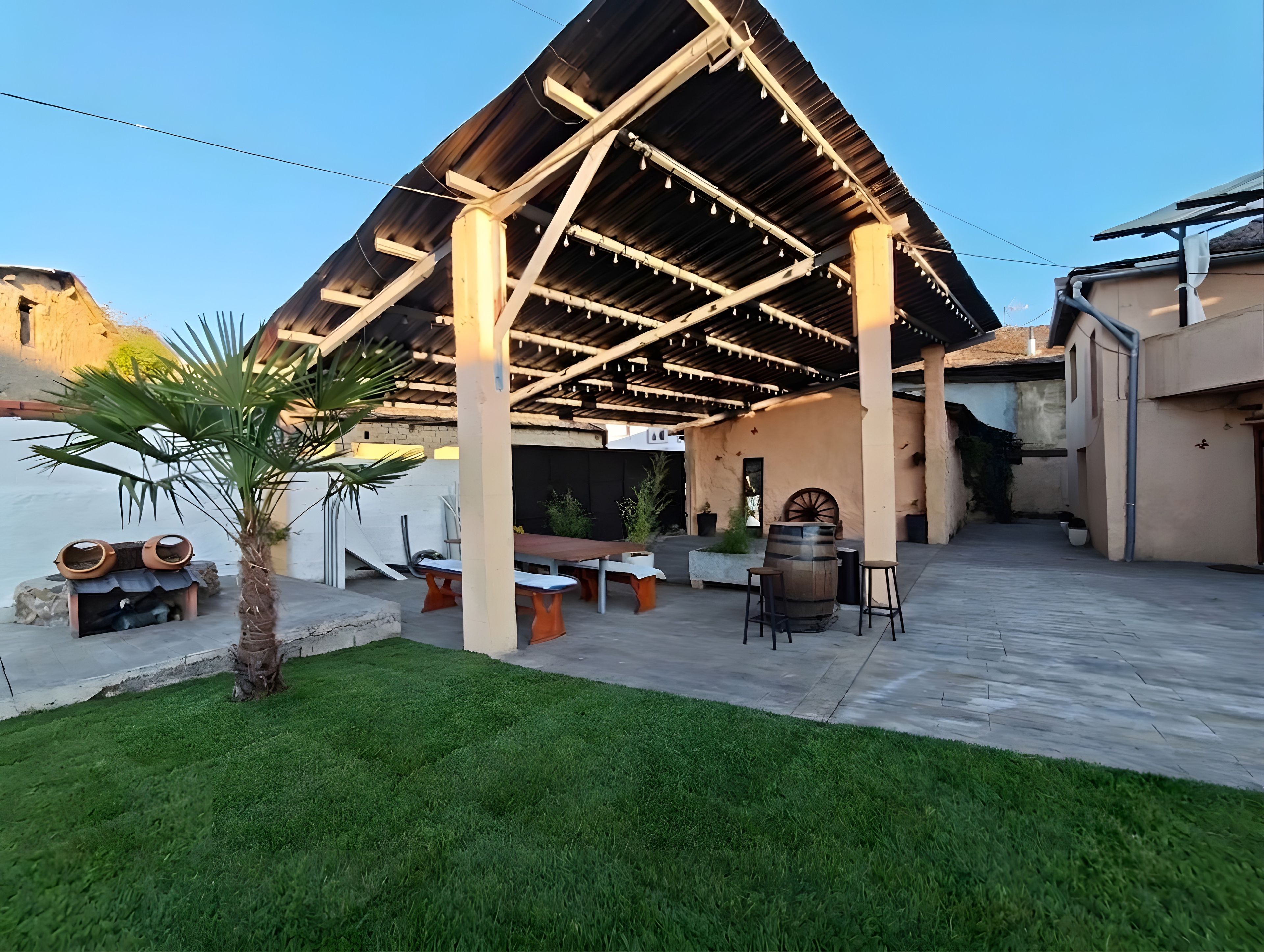 Un área de patio exterior con una estructura de pérgola, arreglos de asientos y una palmera.