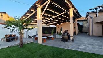 Un área de patio exterior con una estructura de pérgola, arreglos de asientos y una palmera.