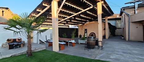 An outdoor patio area with a pergola structure, seating arrangements, and a palm tree.