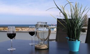 A table with two wine glasses, a glass pitcher, and a potted plant on a balcony overlooking the sea. - Holiday Apartment With 2 Bedrooms (Heiligenhafen)