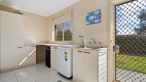 A compact kitchen with a built-in washing machine, a sink, and a window with a view of the outdoors. - 58 Saltwater Crescent (Diamond Beach)