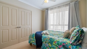 A bedroom with a bed, a window with sheer curtains, a ceiling fan, and a door. - 58 Saltwater Crescent (Diamond Beach)