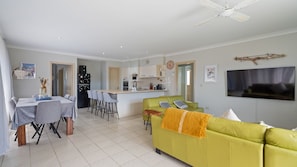 A modern living space with a dining area, kitchen, and a green sofa. - 58 Saltwater Crescent (Diamond Beach)