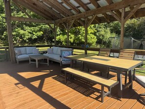Eine Holzterrasse mit überdachter Sitzgelegenheit, einschließlich einer Couch und Tischen.