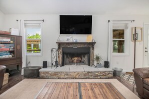 Ein Wohnzimmer mit Kamin aus Stein, einem darüber montierten Flachbildfernseher und Holzboden.