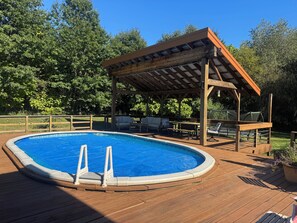 Eine Holzterrasse mit Pool, Gartenmöbeln und einem überdachten Sitzbereich.