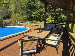 Eine Holzterrasse mit Pool, Sitzgelegenheiten im Freien und einem überdachten Bereich.