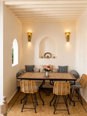 Un coin repas comprenant une table rectangulaire, quatre chaises en osier, deux appliques murales et une assiette décorative accrochée au mur.