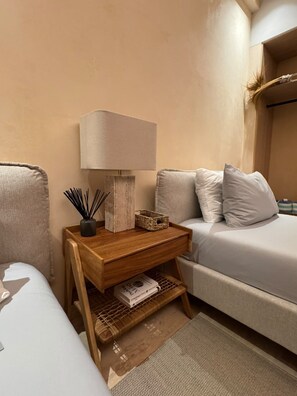 Ein ordentlich eingerichtetes Schlafzimmer mit Bett, Nachttisch, Lampe und einem kleinen Regal mit Büchern und Dekoration.