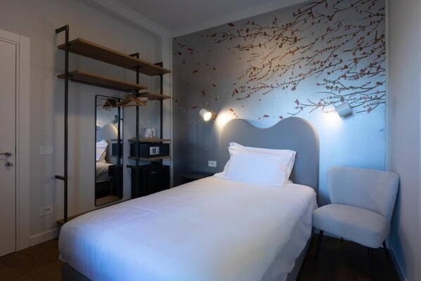 A bedroom with a bed, a chair, a wardrobe, and a wall with a branch design.
