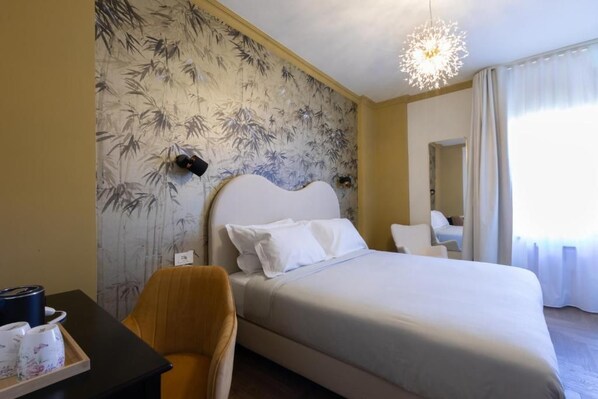 A hotel room with a bed, a chair, a desk with a tray of items, and a wall with a bamboo pattern.