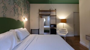 Una habitación de hotel con cama, sillón, escritorio, lámpara y armario.