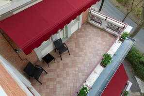 A rooftop terrace with a red awning, two chairs, a small table, and a potted plant.