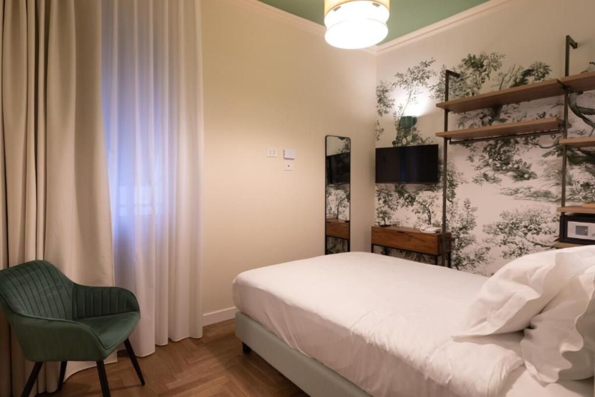 A bedroom with a bed, a chair, a television, and a wall-mounted shelf.