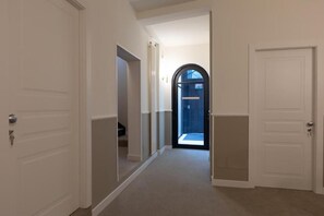 A hallway with white doors, a carpeted floor, and a view into a room with a window.