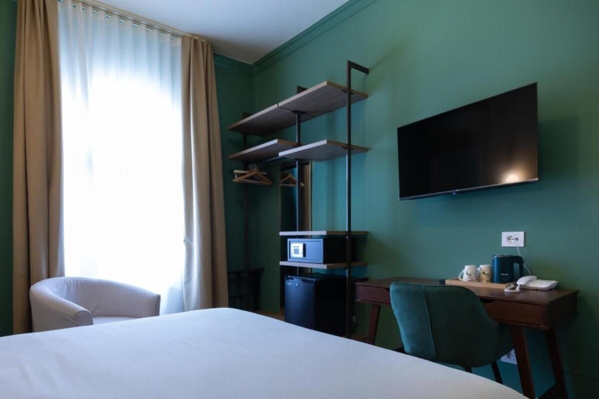 A hotel room with a bed, a desk, a chair, a television, and a wardrobe with shelves.