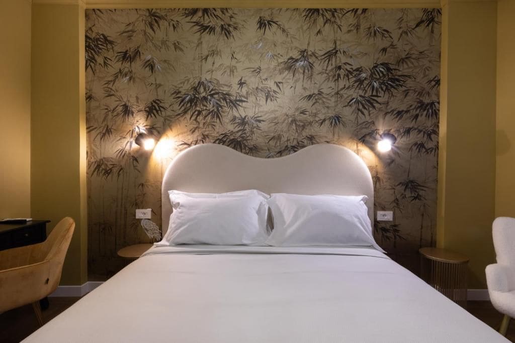 A neatly made bed with white linens in a room with a bamboo wallpaper design.