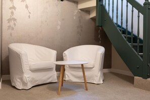A room with a staircase, two white chairs, and a small table.